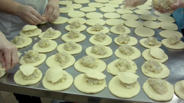 Moulded by hand pies with meat. Female hand, white dough and stuffing balls