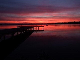 Steg am Ammersee bei Sonnenuntergang, rötlich gefärbtes Wasser 