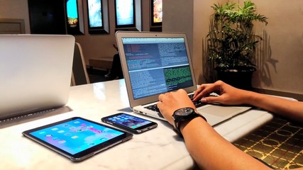 People working, writing some code in his notebook at some office or cozy room, and there is a phone and tablet in his side