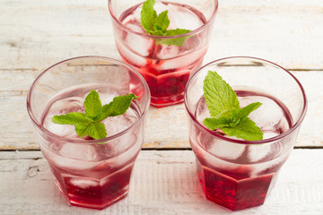 red cocktail with mint and ice in a glass on a wooden background