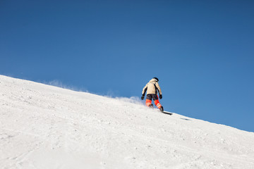 snowboarder going down on white snow slope against clear blue sky background