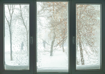 Fototapeta na wymiar window in russian flat with snow blizzard and trees