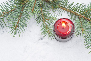 Burning candle on snow with fir branch