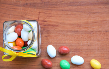 jar of assorted confetti, candies with almond and sugar in different tastes on wooden background 
