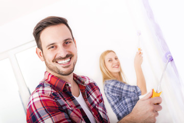 Young smilling couple painting wall in their new house. Home, moving, painting and renovating concept