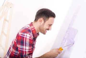 Young smilling man painting wall in their new house. Home, moving, painting and renovating concept