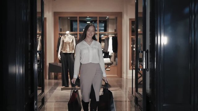 Woman coming out of the clothes store with bags. Girl go from entrance of luxury shop in mall.