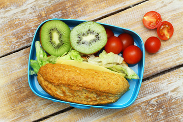 Packed lunch with brown cheese sandwich, cherry tomatoes and two kiwi halves
