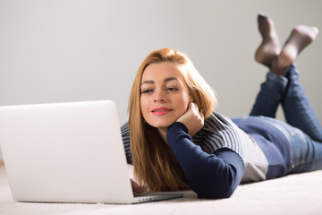 Beautiful woman lying on her floor at home and using notebook