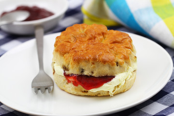 English scone with traditional clotted cream and strawberry jam on white plate
