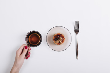 Cup of tea, cake and fork on a white table, a female hand with r