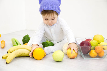 Fototapeta premium The babe in an environment of the fresh vegetables, isolated on the white