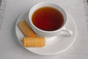Brown beverage in the Cup. Green tea. A Cup of tea. On the plate two wafer rolls. In a white Cup with a saucer tea. A couple of tea. Indian tea. Chinese tea. Studio light