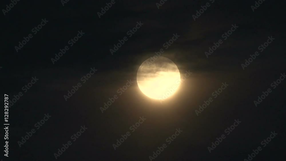 Wall mural full moon rising through clouds, glowing bright in night sky.