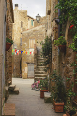 Fototapeta na wymiar Beautiful old stone alley of Pitigliano, Tuscany, Italy during town celebrations with flowers, pennants and a bicycle 