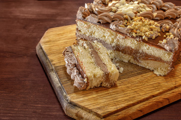 Sliced cake with cream on a round wooden cutting board - closeup