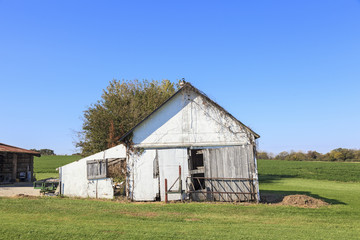 Obraz premium Old wooden shed standing on grass on a country farm with blue sky in the background