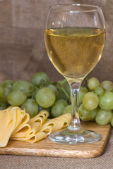 still life with glass of white wine, cheese and grapes on wooden background