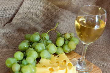 still life with glass of white wine, cheese and grapes on wooden background