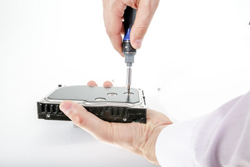 Man's hand holds 3.5 HDD. His another hand unscrews the hard drive case with a screwdriver. Isolated on white background.