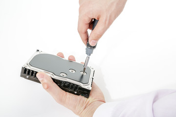 Man's hand holds 3.5 HDD. His another hand unscrews the hard drive case with a screwdriver. Isolated on white background.