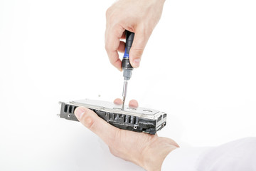 Man's hand holds 3.5 HDD. His another hand unscrews the hard drive case with a screwdriver. Isolated on white background.