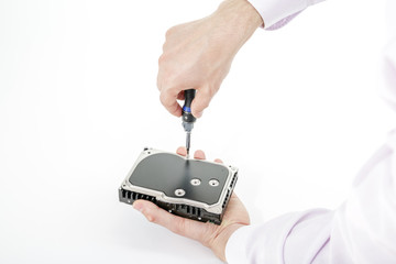 Man's hand holds 3.5 HDD. His another hand unscrews the hard drive case with a screwdriver. Isolated on white background.
