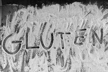 gluten word written in wheat flour on dark board
