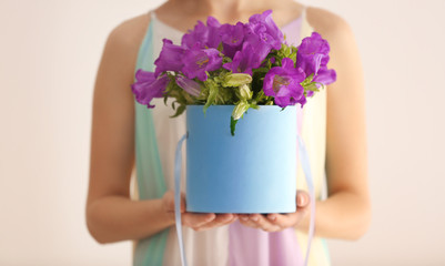Woman holding box with purple bellflowers on light background