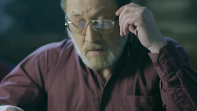 Elderly man with glasses looking away and thinking. Old man reading a book. 