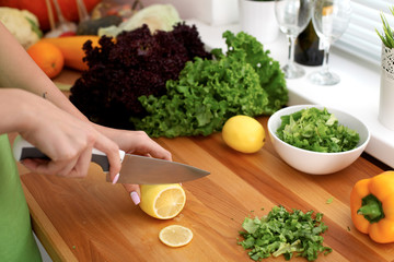 Closeup of woman hands cooking vegetables salad in kitchen. Housewife cuts lemon. Healthy meal and vegetarian concept.