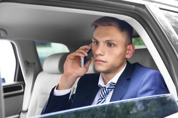 Young businessman sitting in car and talking on phone