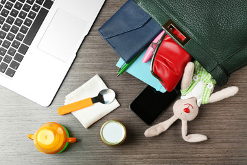 Maternity concept. Female handbag full of different things on office table