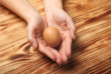 Female hands with egg on wooden background, closeup