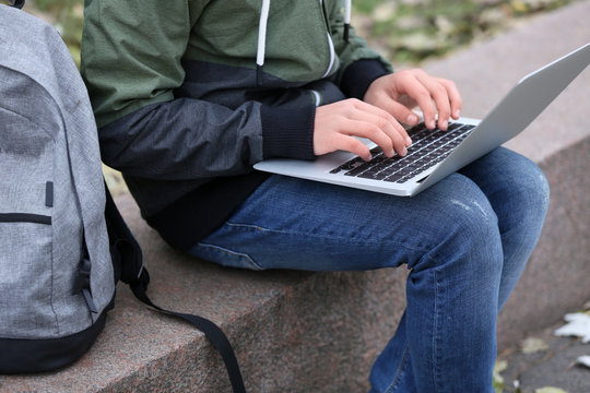 Teenager sitting on parapet with laptop in autumn day, close up