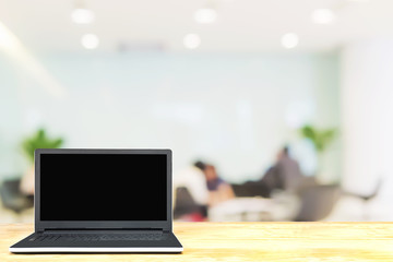 Laptop on white wooden table top over blurred business meeting room with discussing people