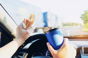 Man is dangerously eating hot dog and cold drink while driving a car