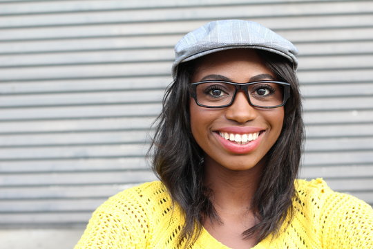 Funky style beauty. Portrait of beautiful young African woman in glasses and funky hat smiling while standing against gray urban background
