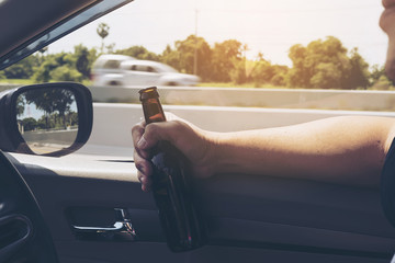 Man holding beer bottle while driving a car