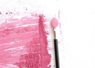 close up of crushed pink color make up with brush on white.