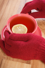 Hand of woman in woolen gloves holding cup of hot tea on table