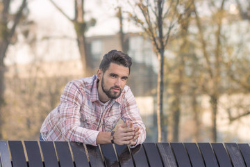 Fototapeta premium Young adult man leaning on bench, outdoors head, face.