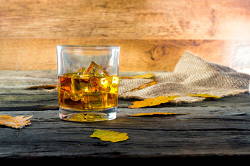 glass of whiskey with ice on a wooden table with oak leaves