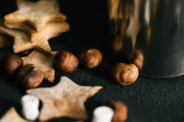 Traditional Christmas star shaped cookies with nuts and marshmallows on black table, close up