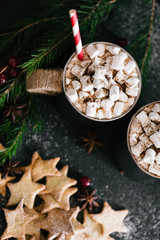 Hot cacao with marshmallows in metal cups, star shaped cookies and red berries on black table