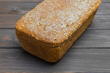 Homemade bread with seeds on dark brown wooden background.