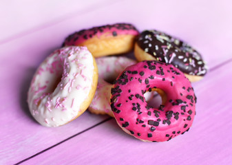 Heap of fresh donuts with glaze on a wooden table. Delicious unhealthy food. Multicolored glazed donuts with chocolate sprinkles.