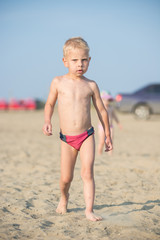 Baby boy walking on the sandy beach near the sea. Cute little kid at sand tropical beach. Ocean coast.