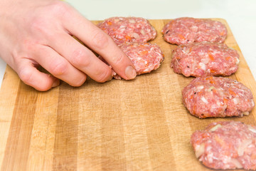 Woman's hand holding mince with grated carrots and onion in there. Cutlets creation on the wooden board in the kitchen. Healthy eating and lifestyle.