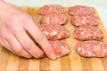 Woman's hand holding mince with grated carrots and onion in there. Cutlets creation on the wooden board in the kitchen. Healthy eating and lifestyle.